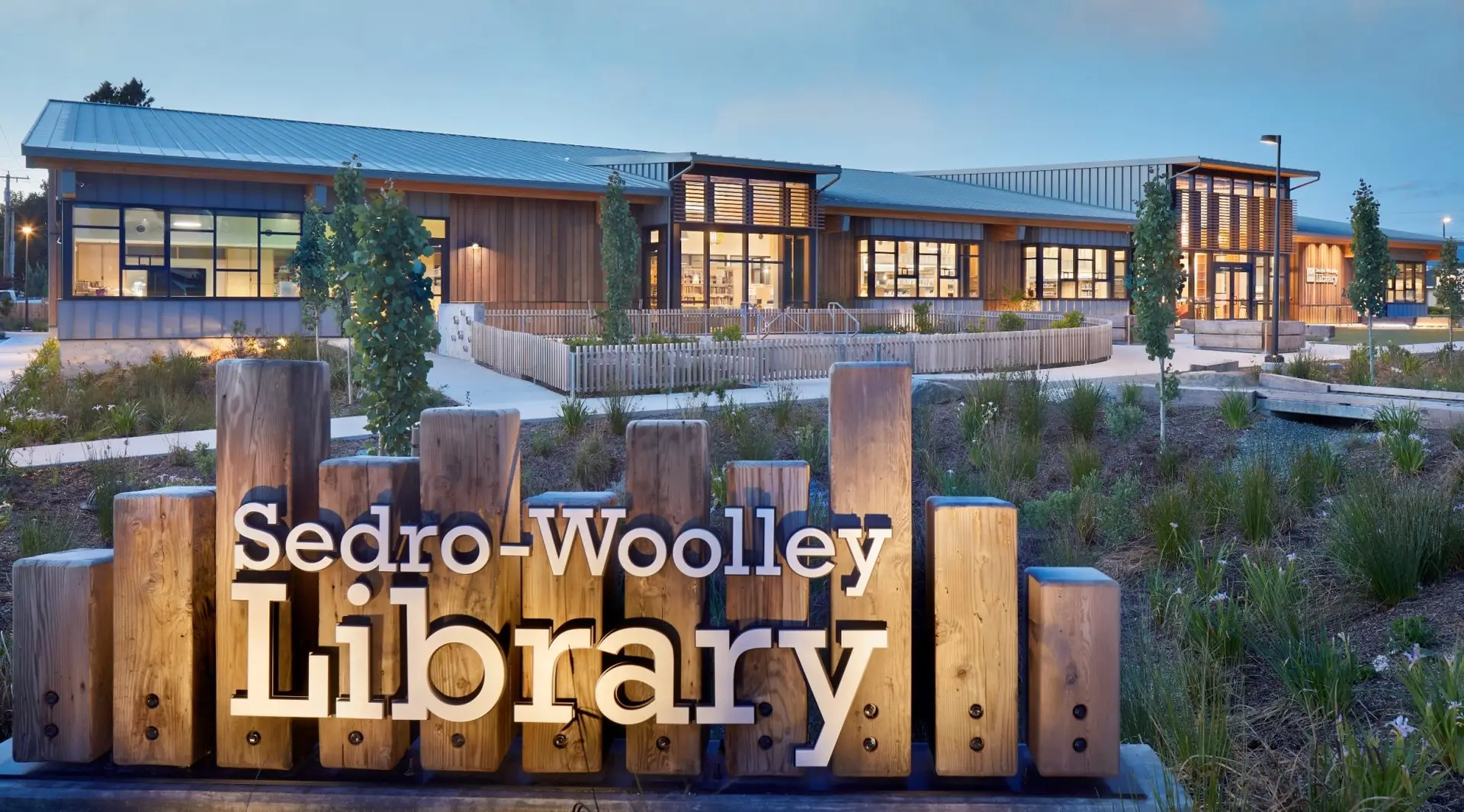 North facing photo of the outside of the Central Skagit Library District building. Forefront is the building sign that reads "Sedro-Woolley Library"